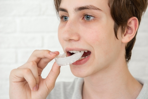 teen,boy,holding,an,silicone,aligner,braces,against,white,studio